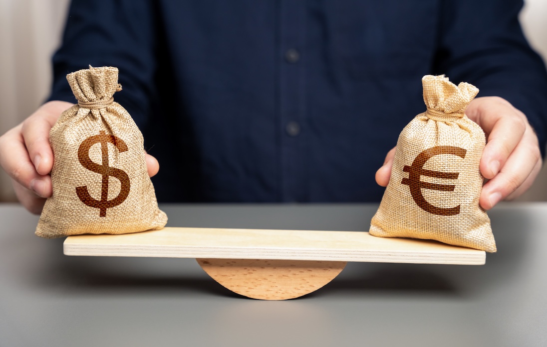 Tafelblad met daarop een soort van houten balansje en een man die twee zakjes vasthoudt met in de een dollars en de andere euro's