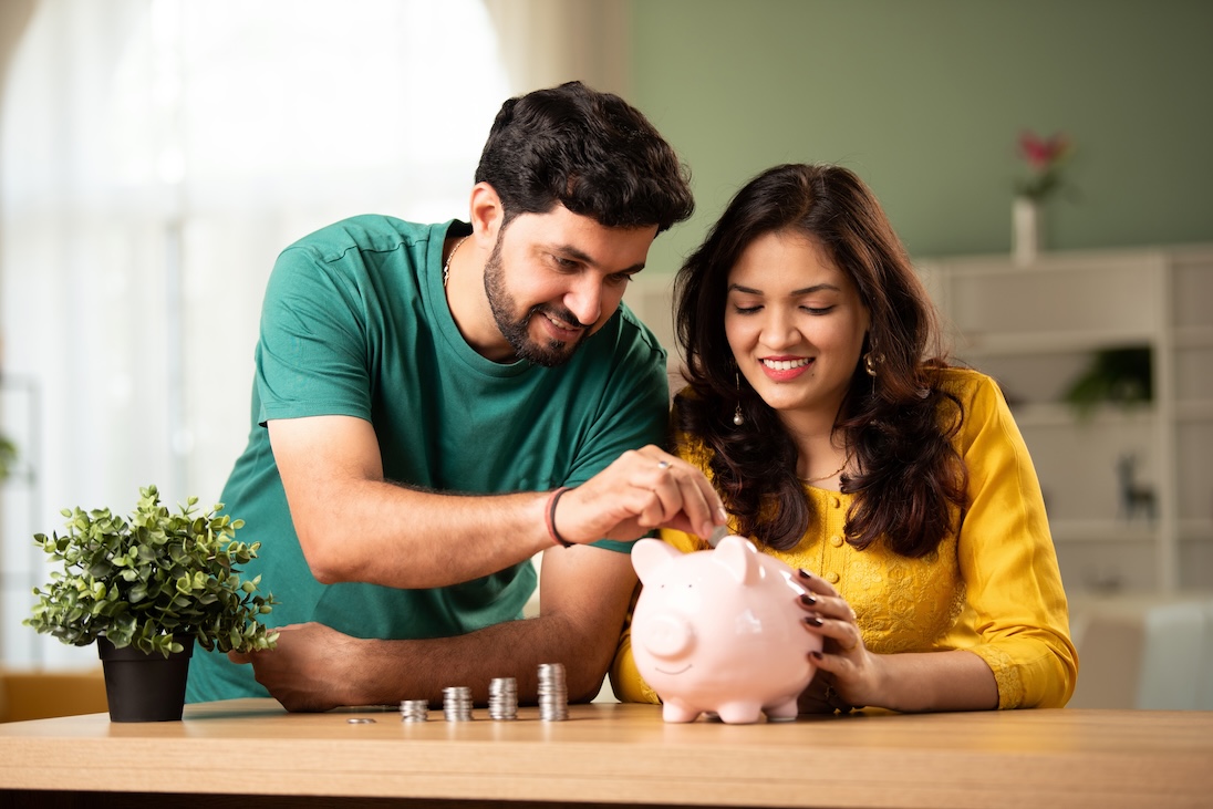Twee personen, een man en een vrouw, die geld in een spaarvarken stoppen