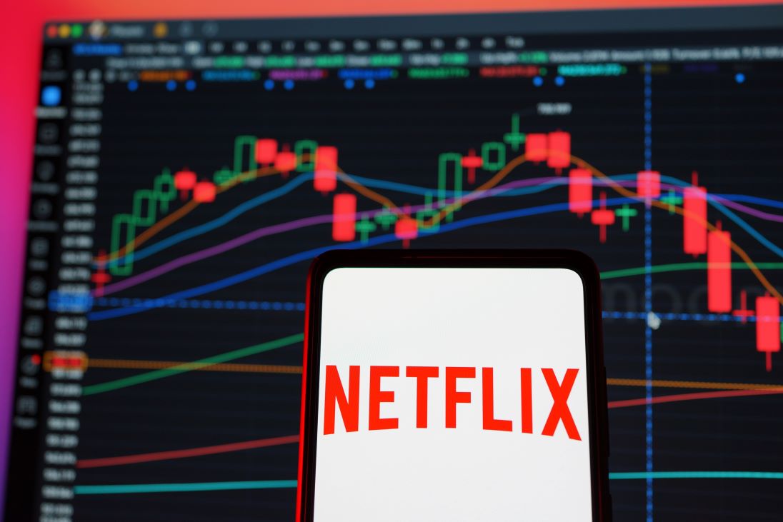 Logo van Netflix op een smartphone en op de achtergrond aandeelkoers overzicht