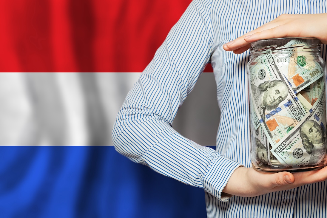 Op achtergrond de vlag van Nederland. Op voorgrond een man die een grote glazen pot vasthoudt waarin veel bankbiljetten zitten